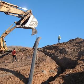 A man is standing on top of a pile of dirt next to a large excavator.