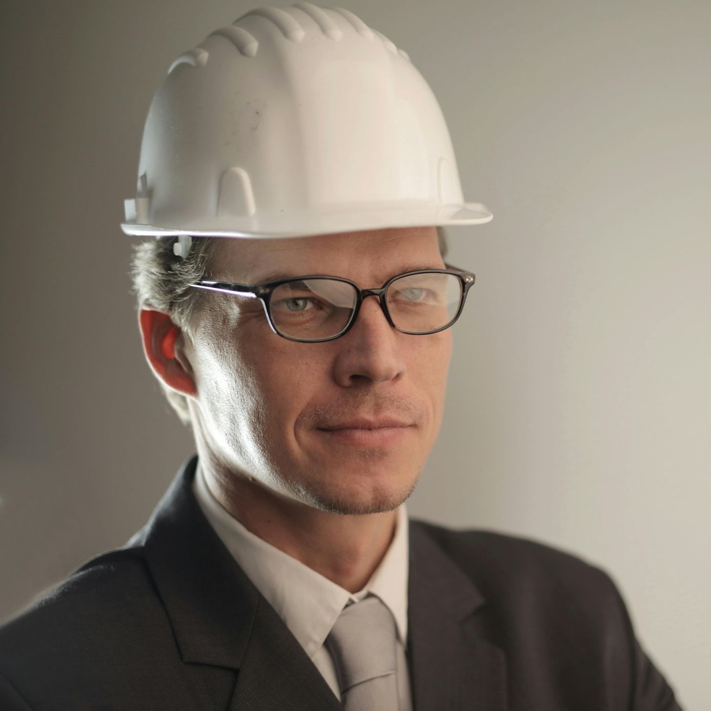 Man in suit and glasses wearing a white hard hat.