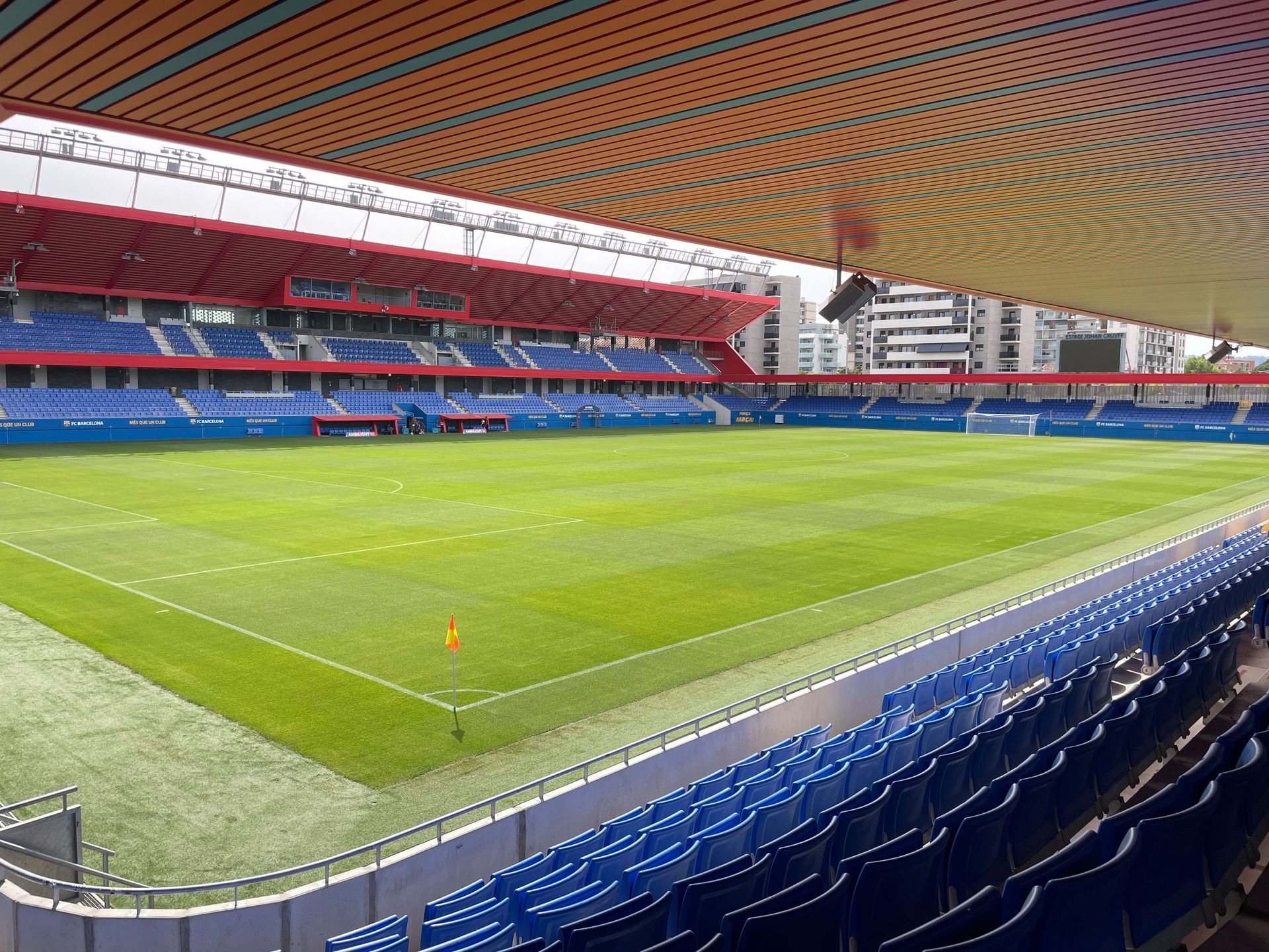 Las gradas azules vacías dan a un campo de fútbol verde. Detalles rojos y azules en las gradas.