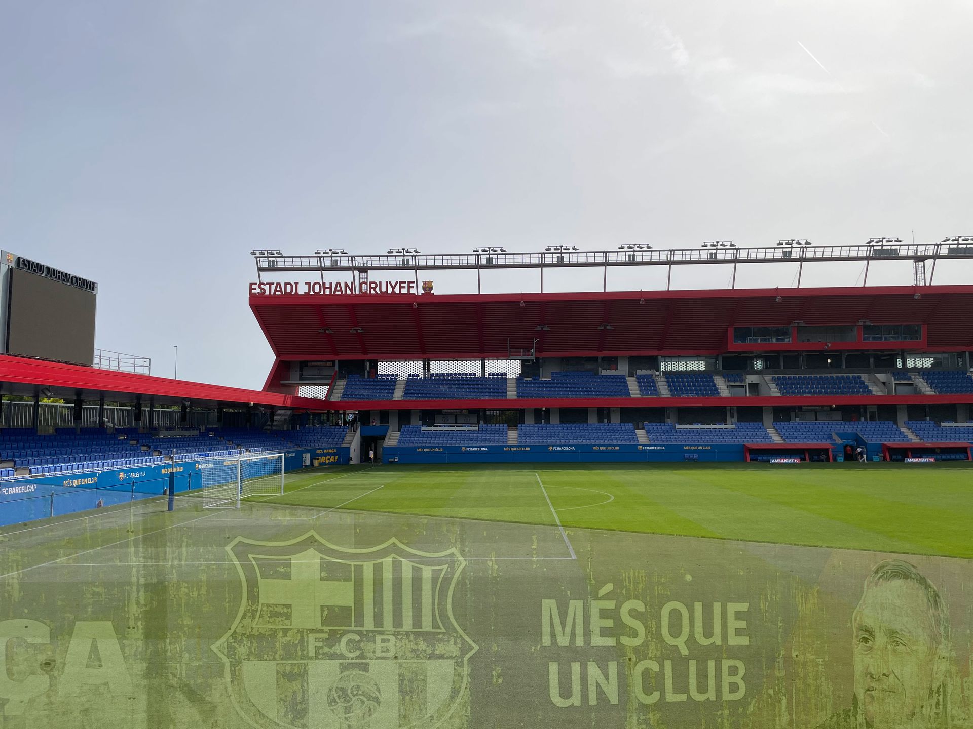 Vista exterior de un estadio de fútbol con asientos rojos y azules, campo verde y un cielo nublado.