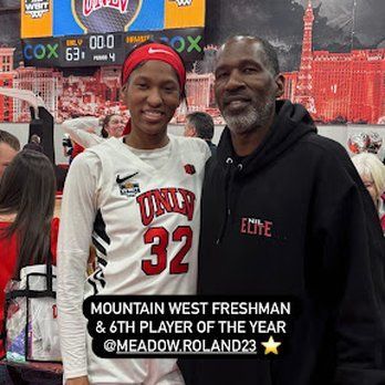 A man and a woman are posing for a picture in front of a scoreboard.