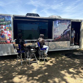 A group of people are sitting in front of a trailer playing video games.