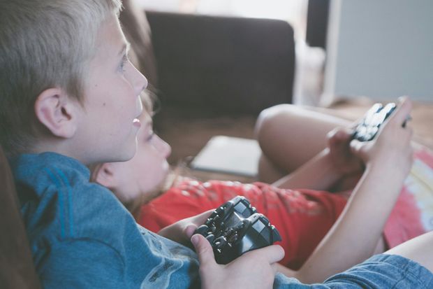 Two young boys are sitting on a couch playing a video game.