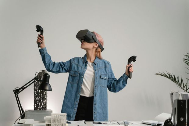 A woman is wearing a virtual reality headset and holding two controllers.