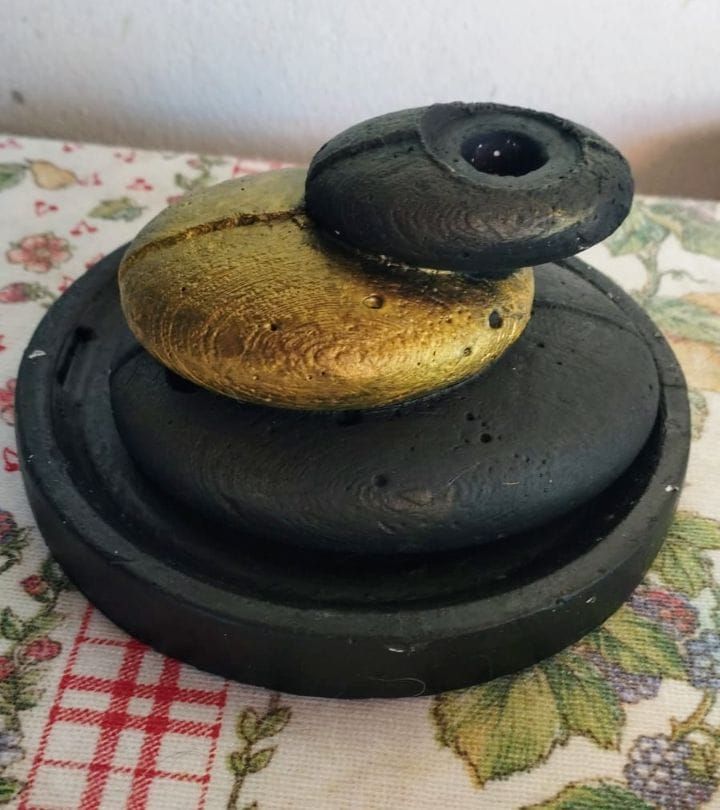 Piedras apiladas y pintadas en negro, dorado y azul oscuro sobre una superficie estampada.