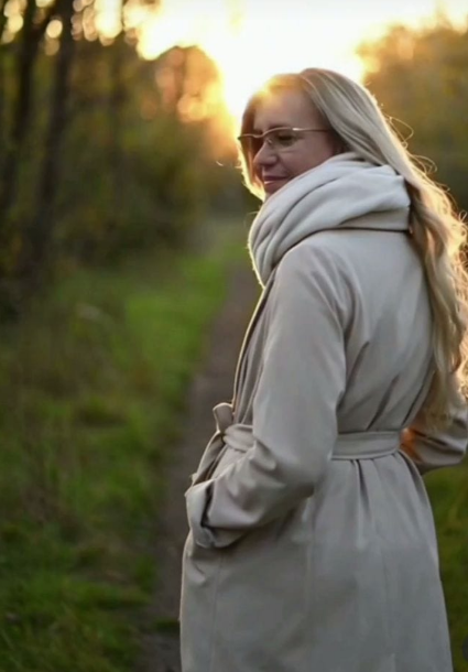 Mujer con gafas, apoya la barbilla en la mano y sonríe. Cabello rubio, con chaqueta negra en el interior.