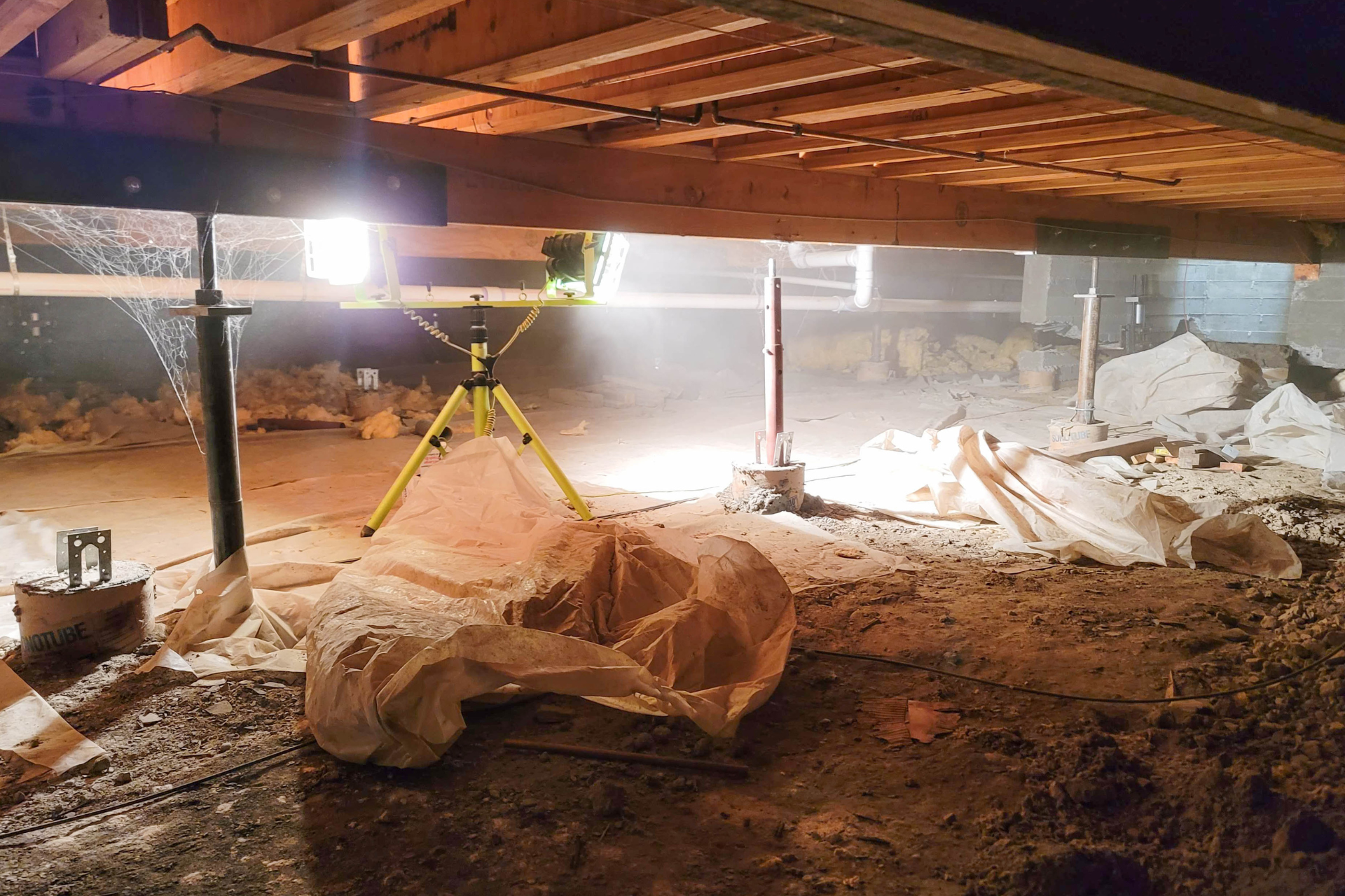 A tripod is sitting underneath a wooden floor in a basement.