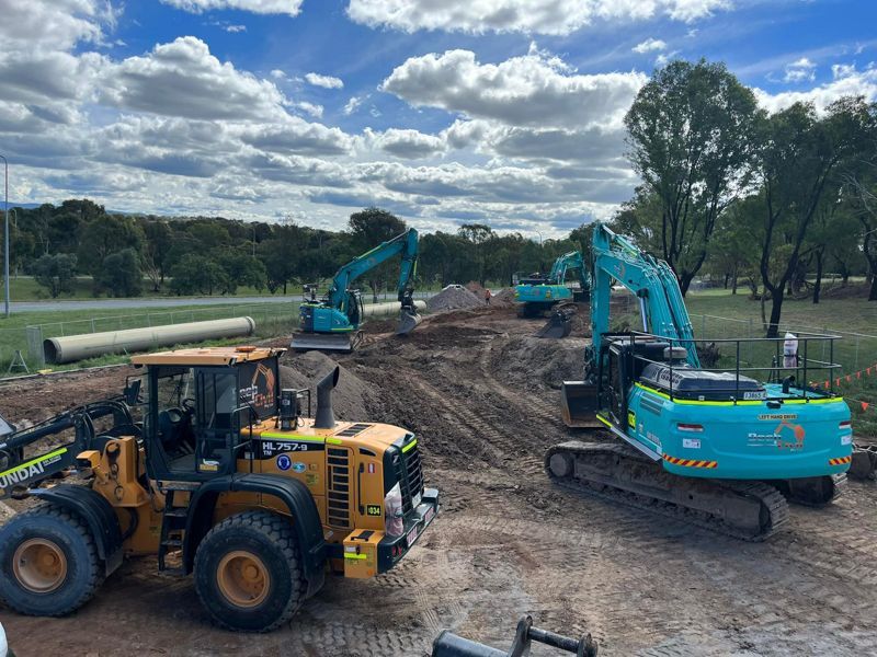 A group of construction vehicles are sitting on top of a dirt field.