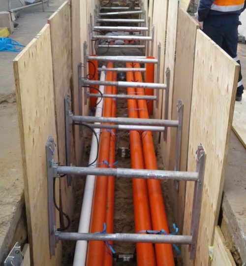 A row of orange pipes are being installed in a trench.
