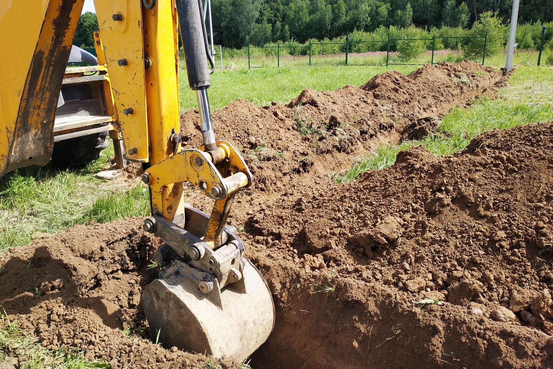 Yellow backhoe digging a trench in a grassy field.