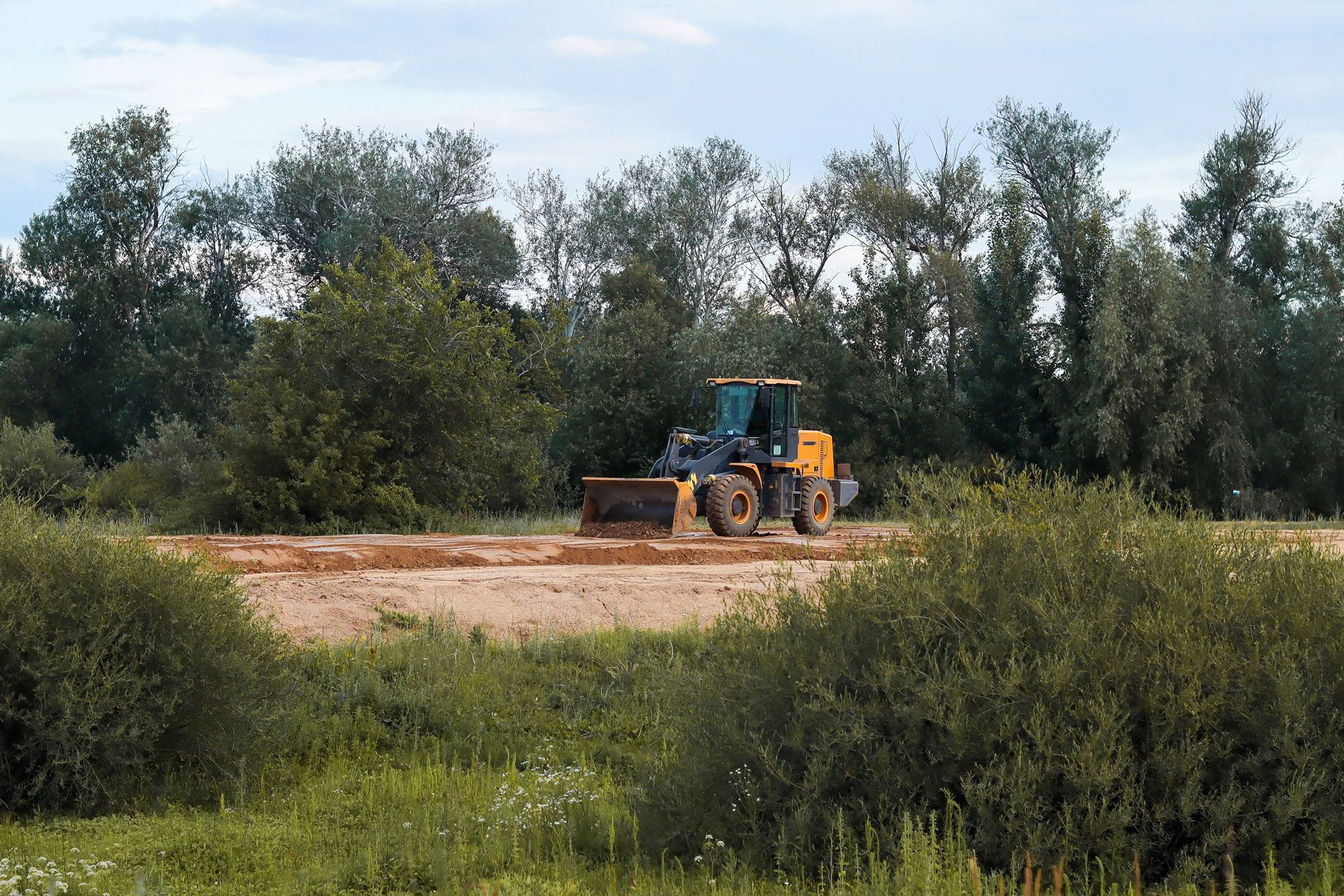 Yellow bulldozer clearing land in a green, wooded area.