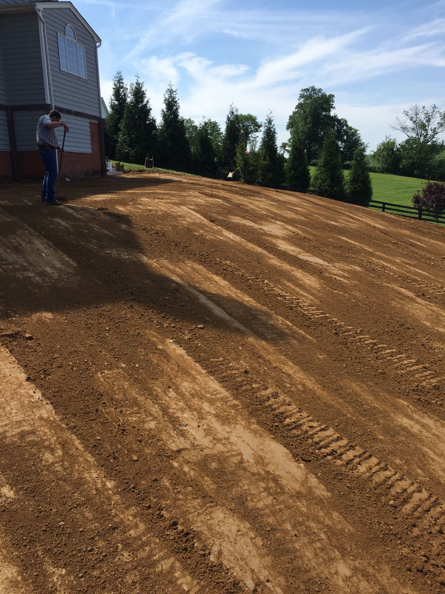 A man is standing in a dirt field in front of a house.