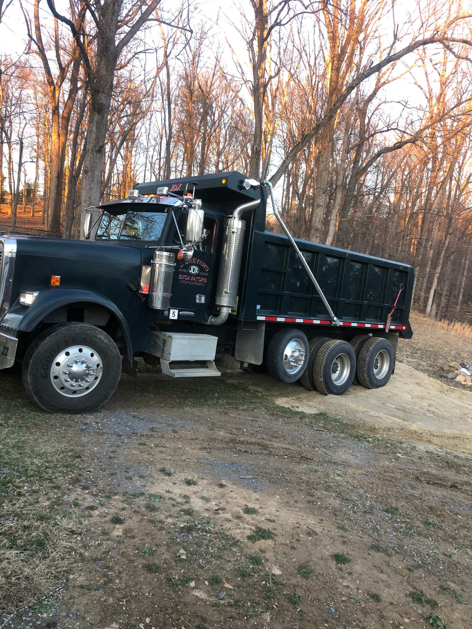A black dump truck is parked on the side of a dirt road.