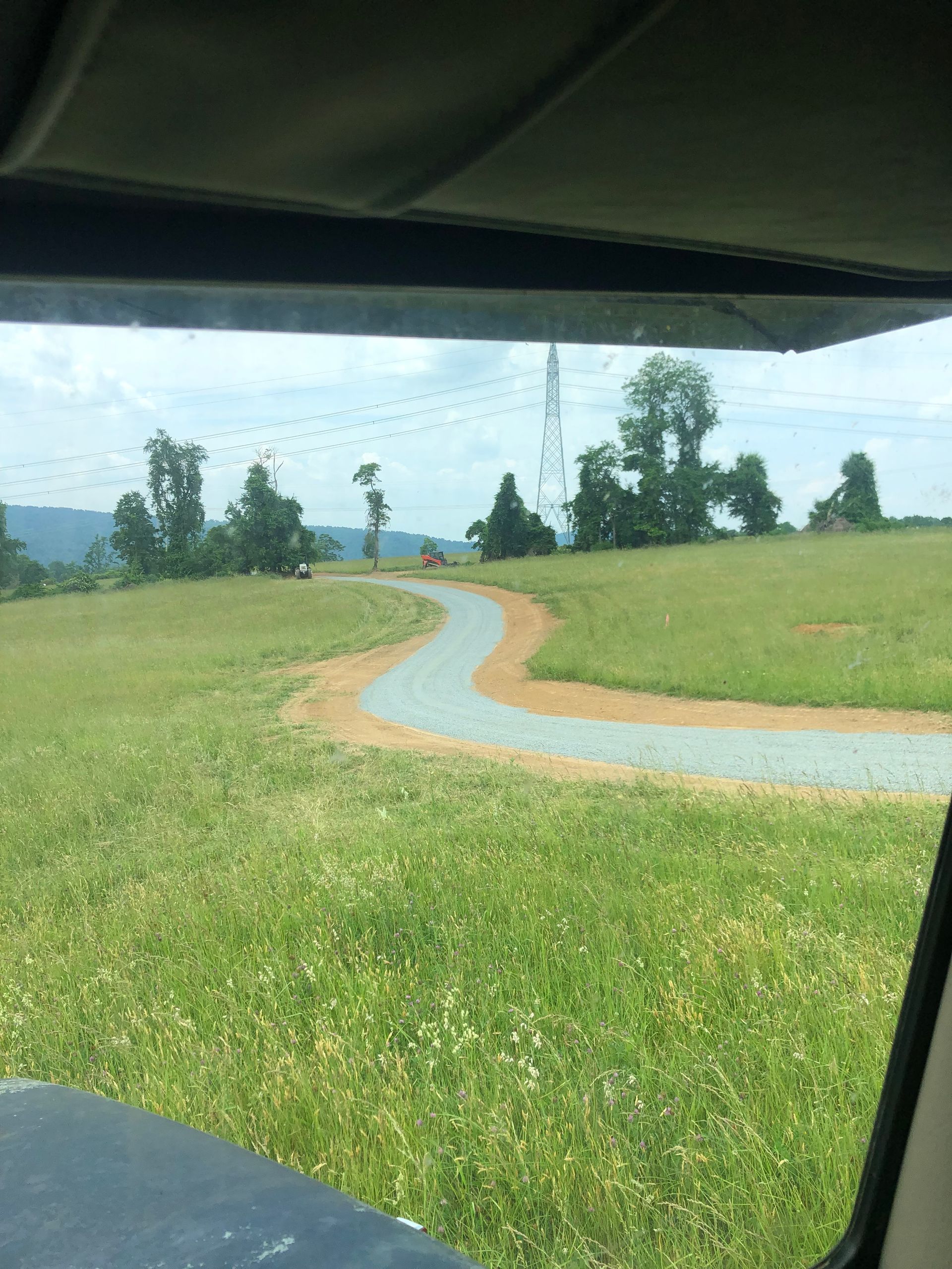 A car is driving down a dirt road through a grassy field.