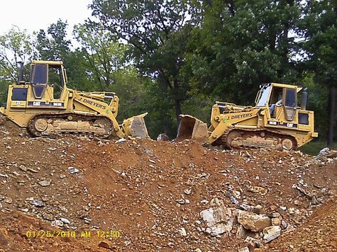 Two bulldozers are parked on top of a dirt hill