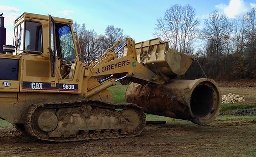 A bulldozer is moving a large pipe in a field.