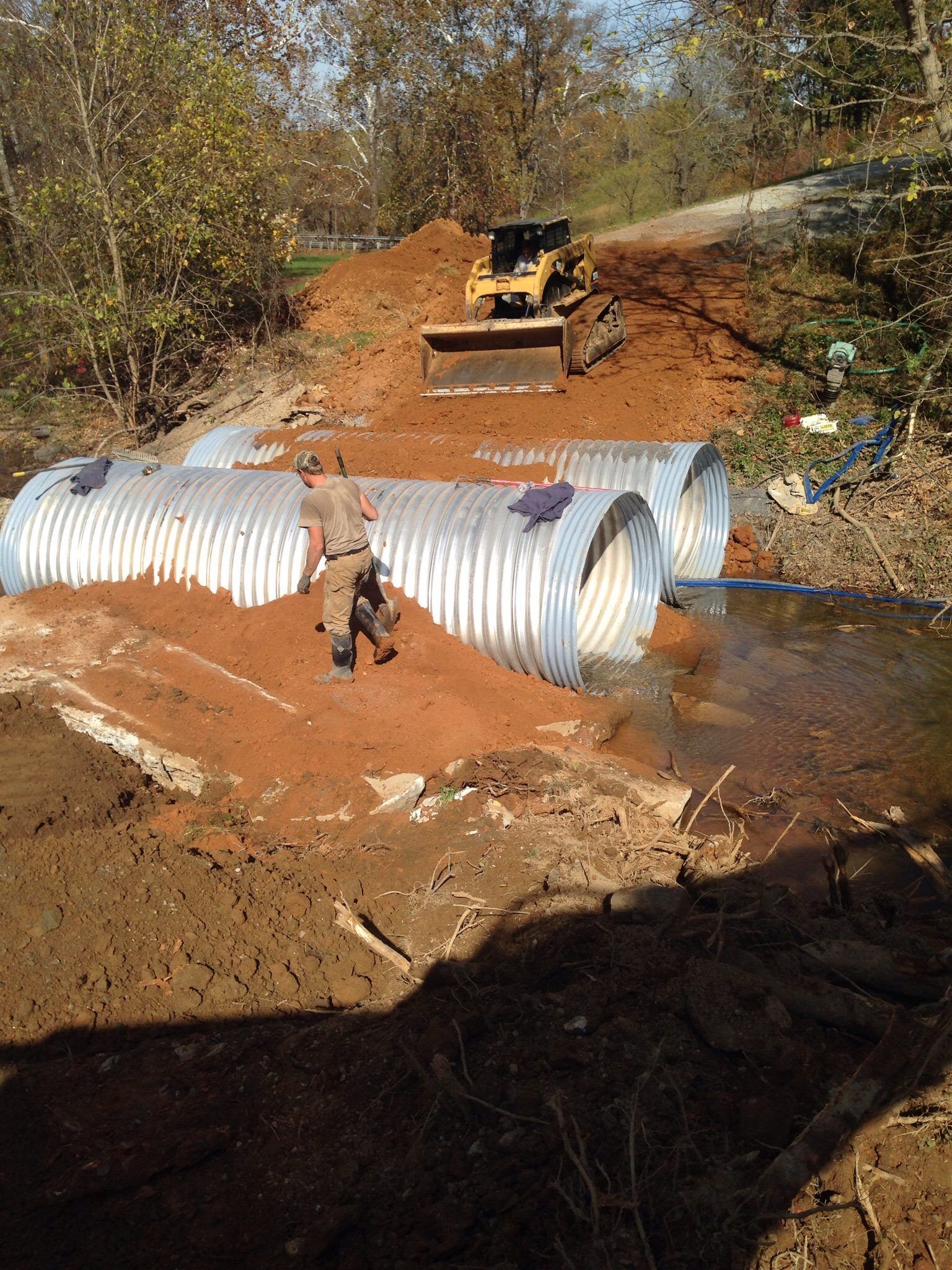 A man is standing next to a large metal pipe in the middle of a river.