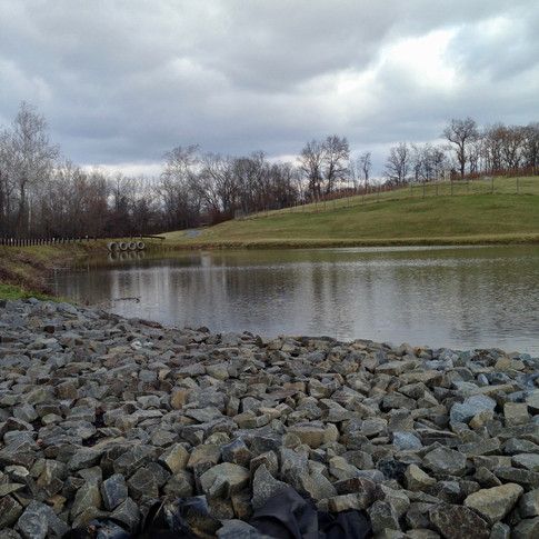 A lake surrounded by rocks and grass on a cloudy day