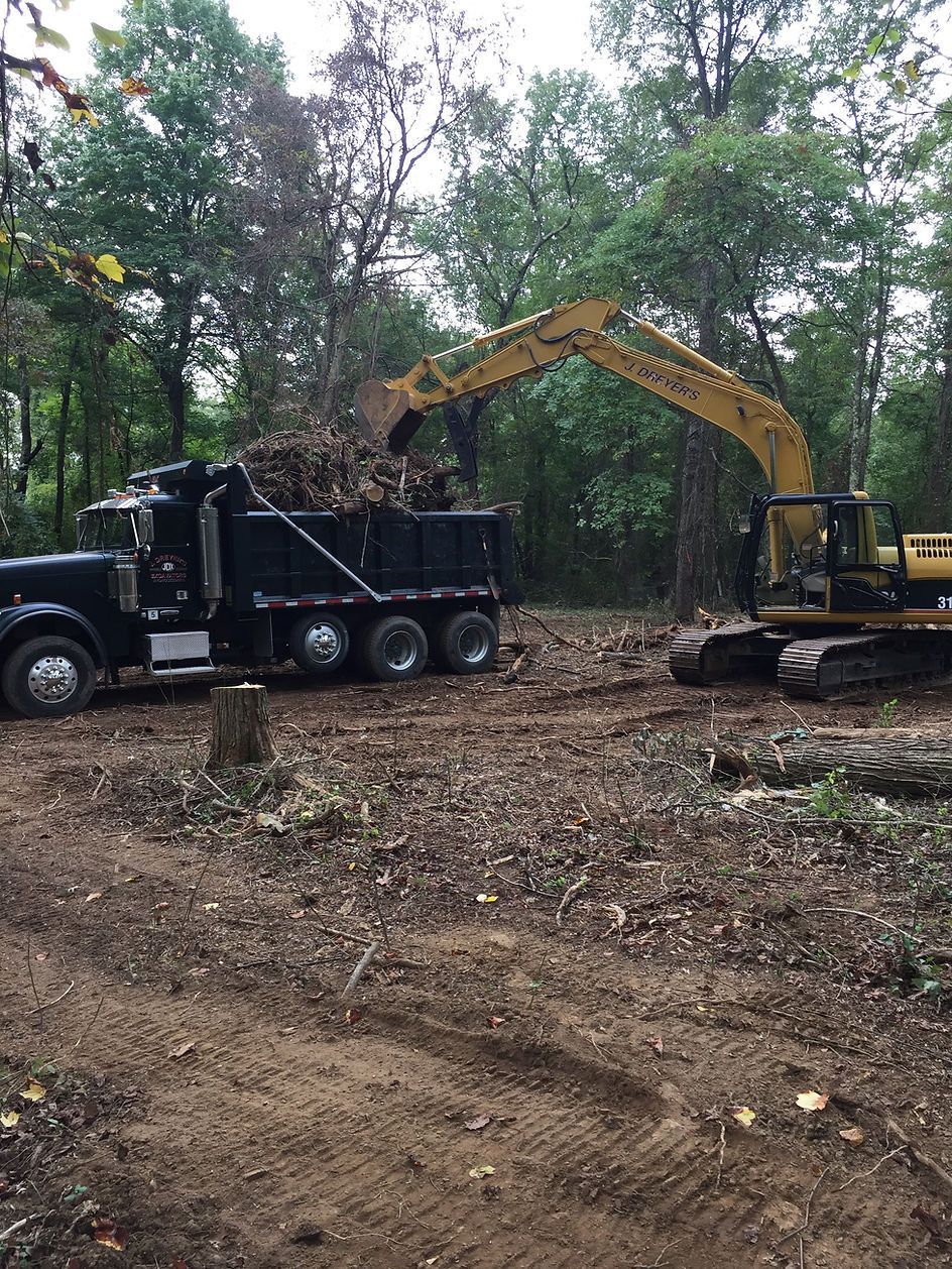A dump truck is being loaded with logs by an excavator.