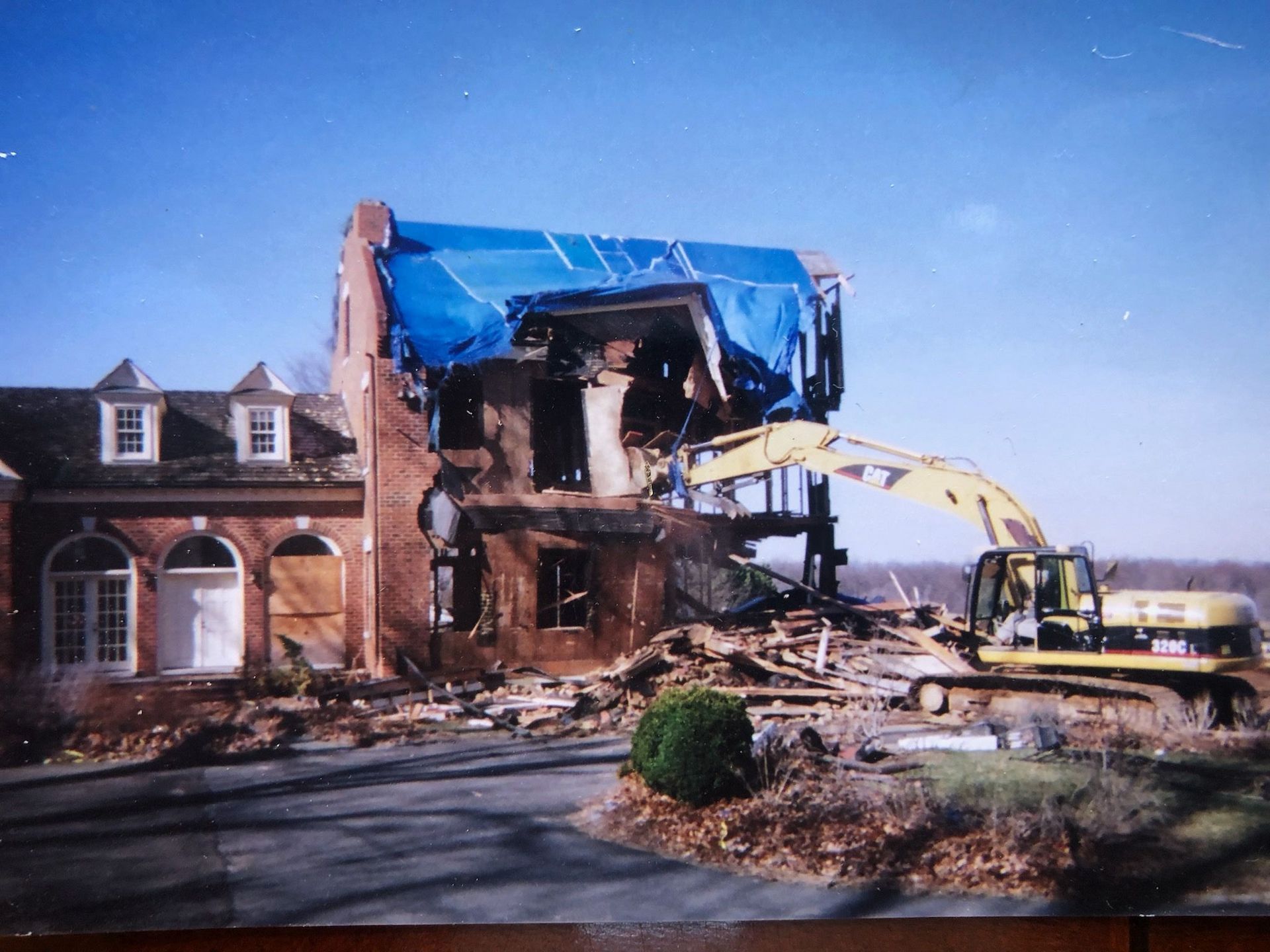 A yellow bulldozer is demolishing a house in the middle of a field.
