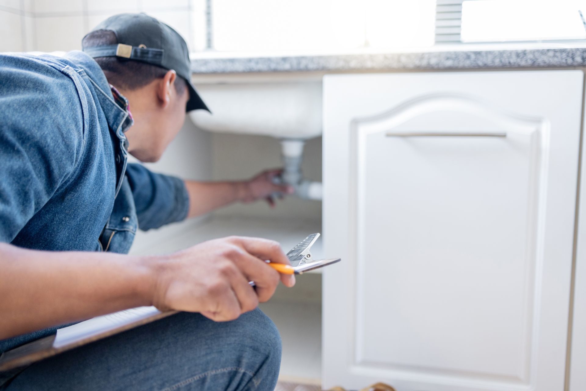 Plumber inspecting and repairing sink pipes under kitchen cabinet.