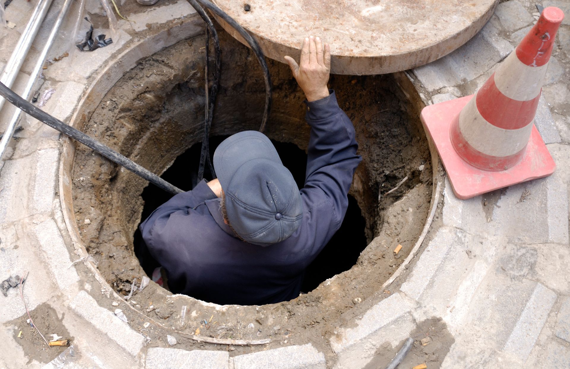 A man in a hole repairing a drain as part of essential emergency sewer cleaning work.