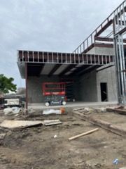 Construction site: metal building frame with a red lift inside a covered area. Cloudy sky.