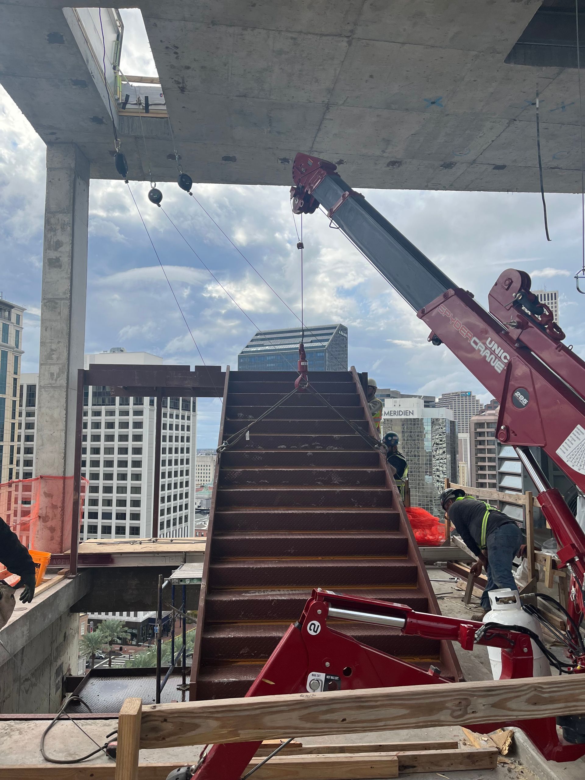 Steel frame of a building under construction. Workers in safety vests are visible.