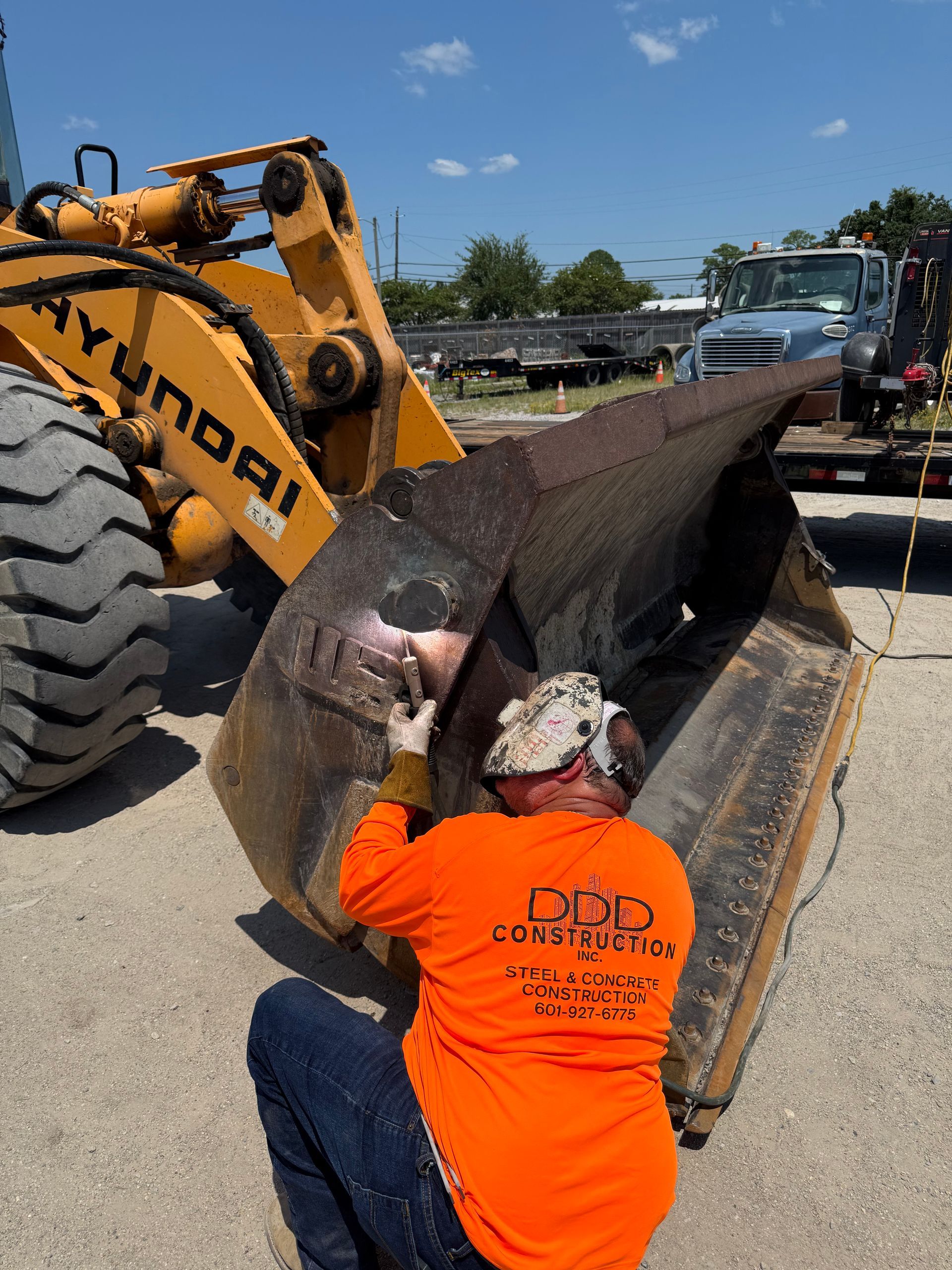 Yellow forklift arm inside a building, with construction vehicles in background.
