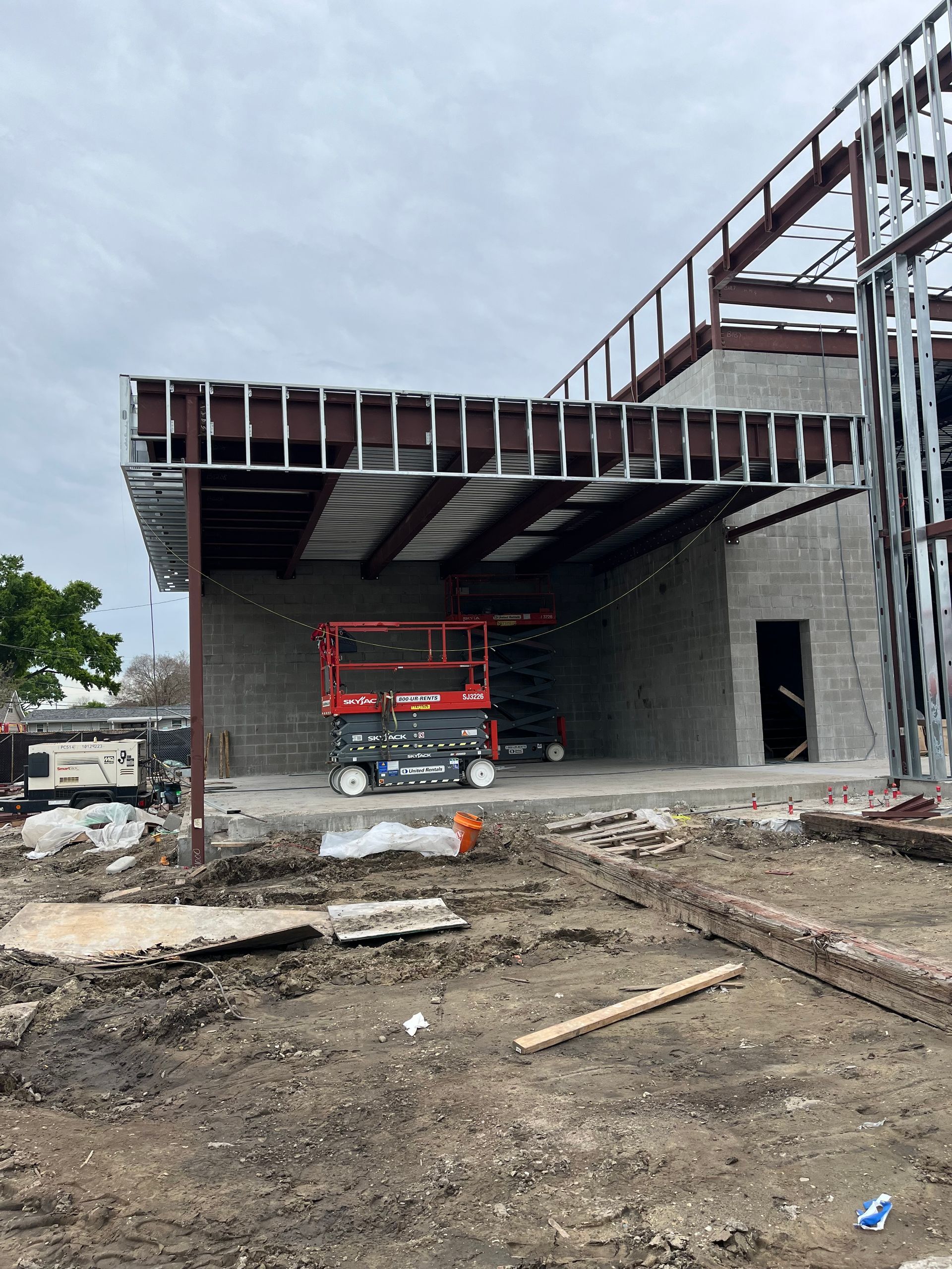 A person in orange shirt working on yellow heavy machinery, outdoors, in front of garage.