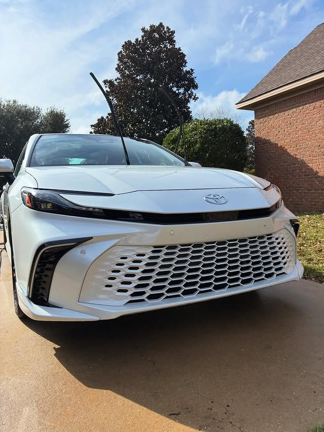 A white Toyota Crown parked on a driveway in front of a brick house under a blue sky.