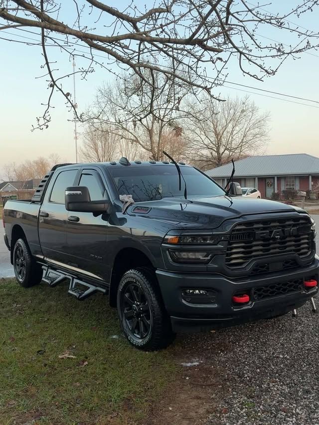 A dark gray RAM pickup truck parked on a grass and gravel lot under tree branches near a house.