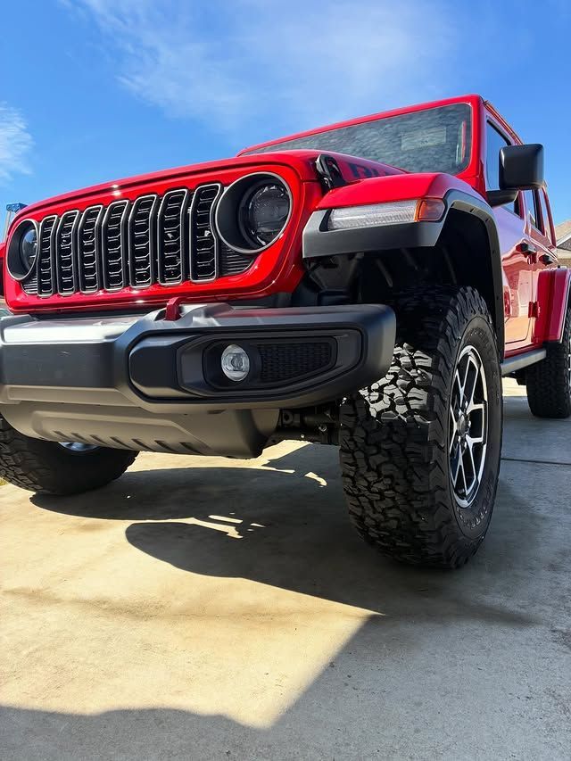 A low-angle view of a bright red Jeep Wrangler parked on a concrete surface under a clear blue sky.