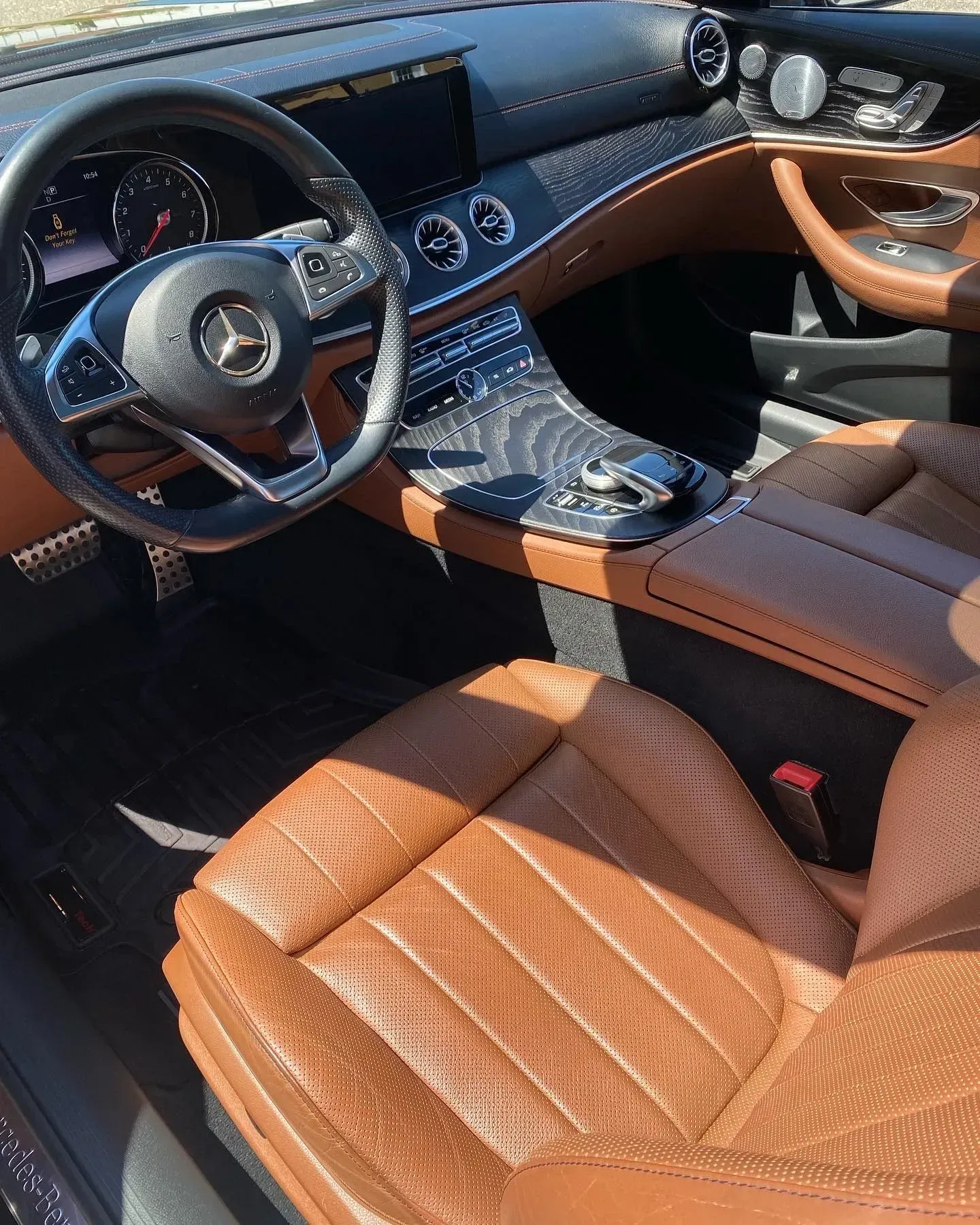 Interior view of a Mercedes-Benz car with tan perforated leather seats, a dark dashboard, and a multi-function steering.