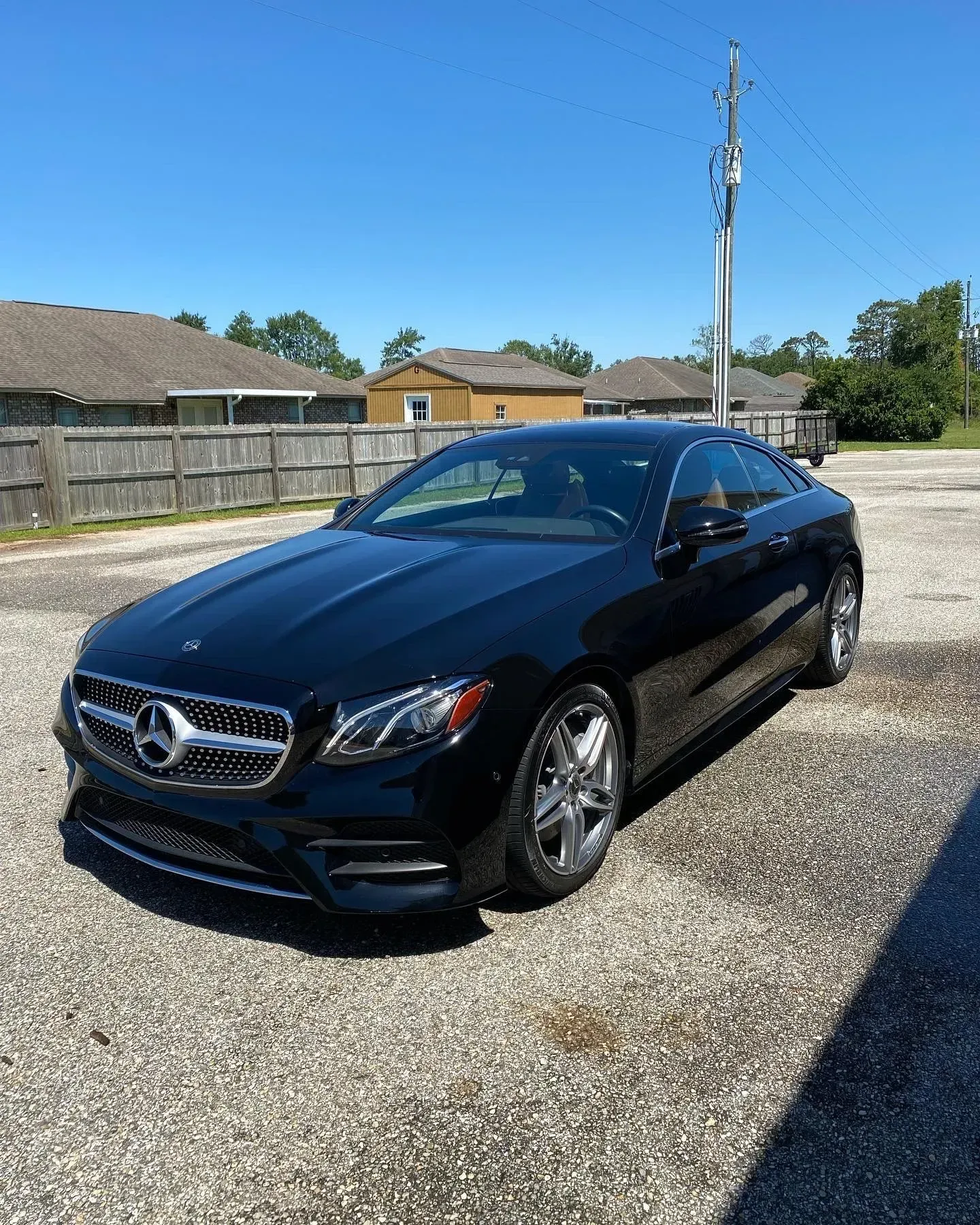 A black Mercedes-Benz E-Class coupe parked on a gravel lot under a clear blue sky.