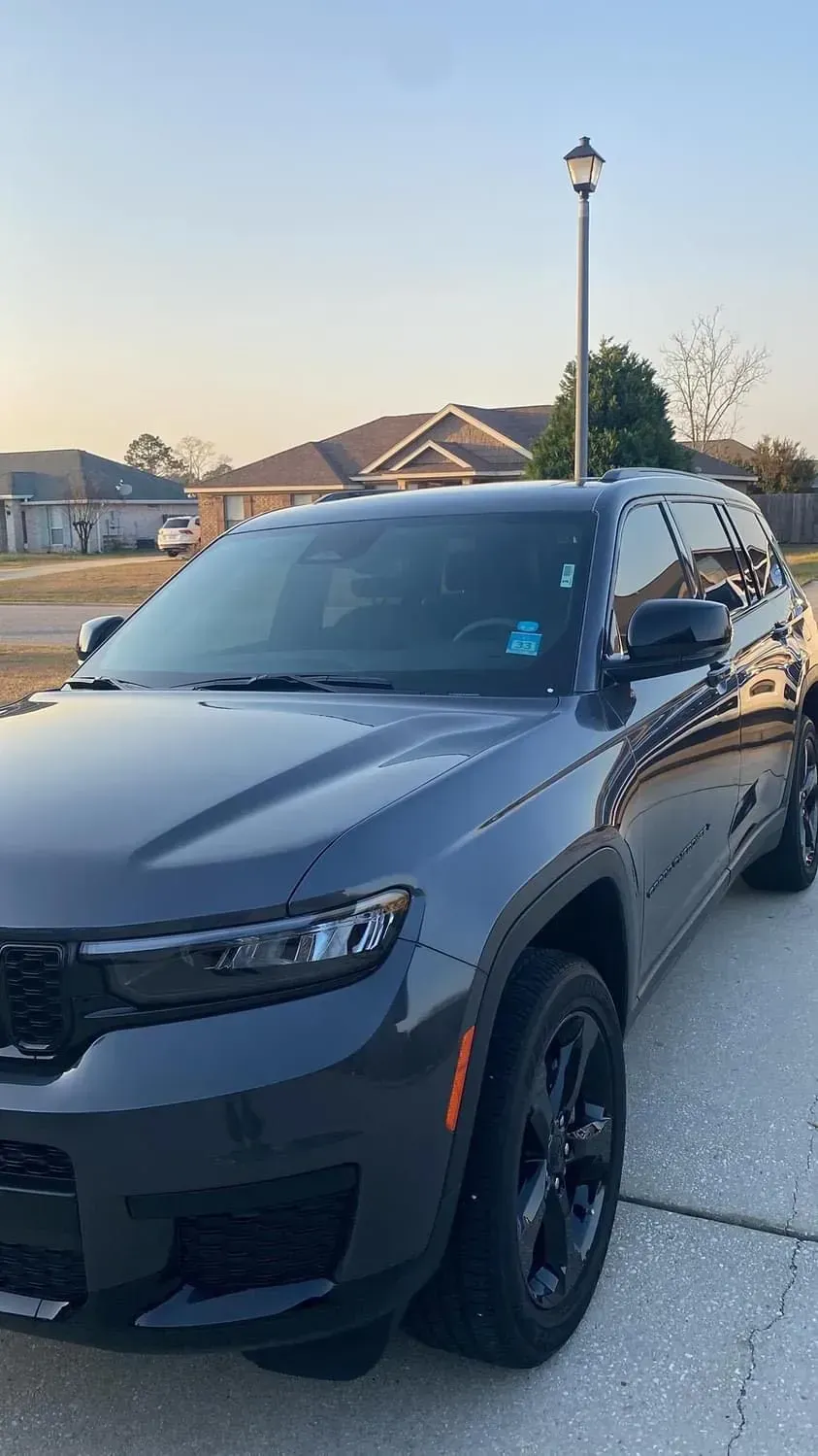 A dark gray Jeep Grand Cherokee parked on a concrete driveway in a suburban neighborhood at sunset.