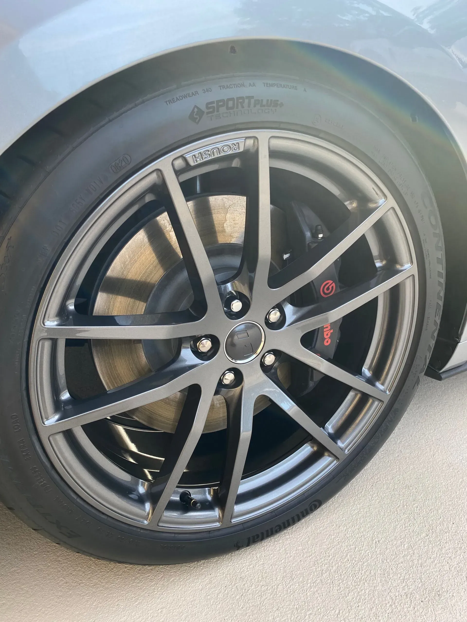 Close-up view of a dark grey multi-spoke car wheel with a Brembo brake caliper visible against a light grey car body.