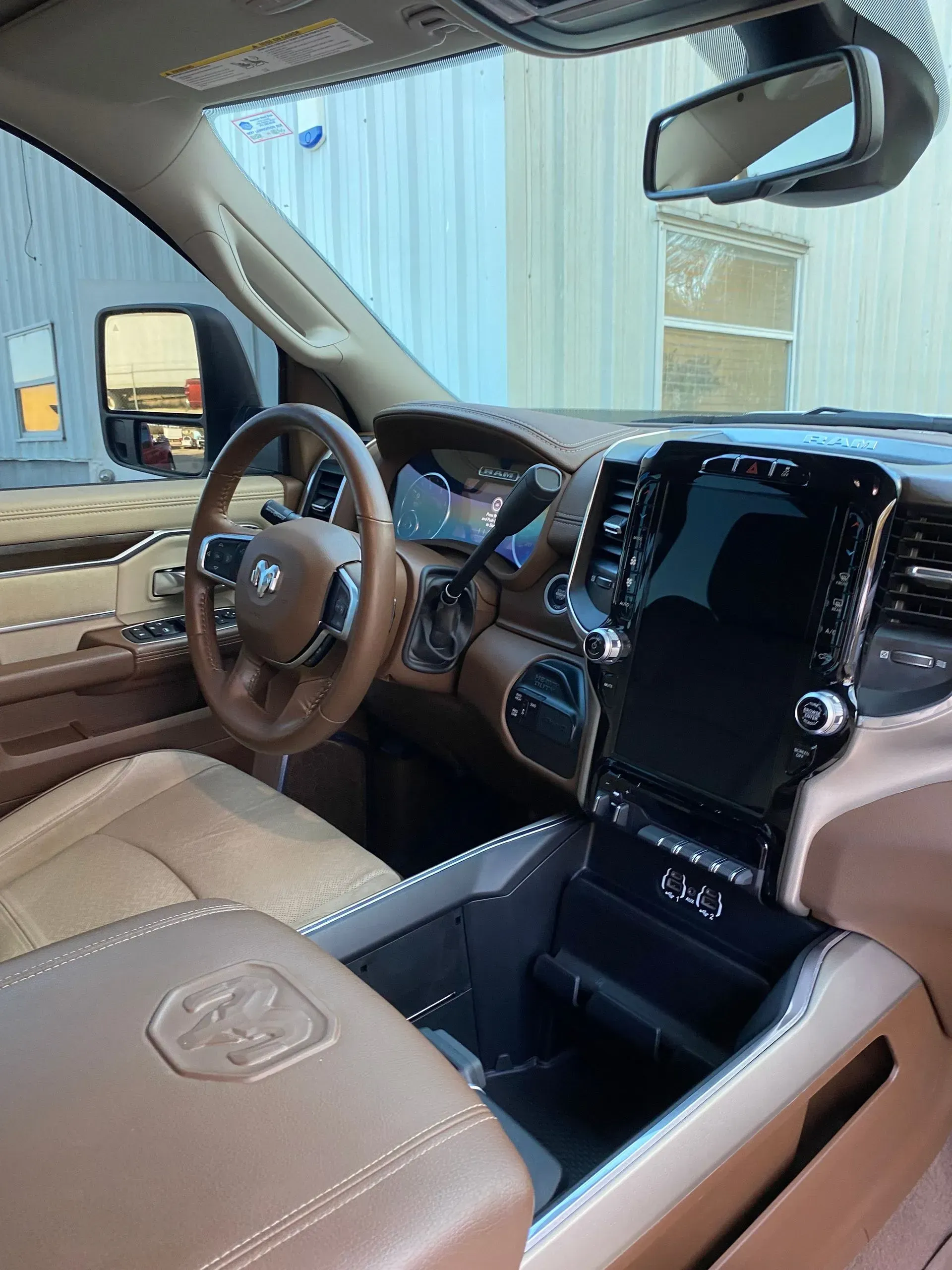 The interior of a modern vehicle, featuring tan leather seats, a large vertical touchscreen, and a branded steering wheel.
