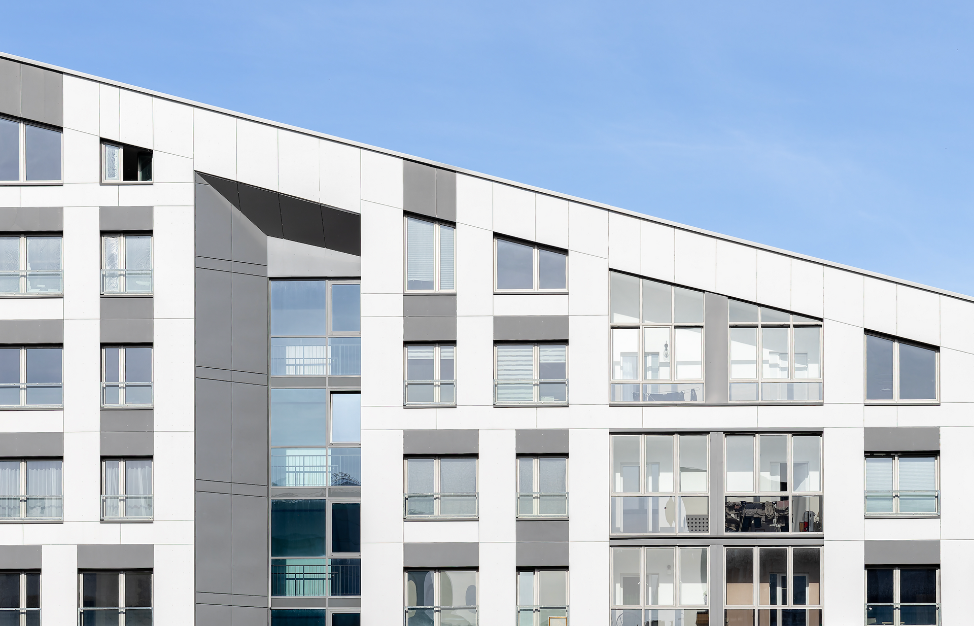 White and gray modern building with many windows against a clear blue sky.