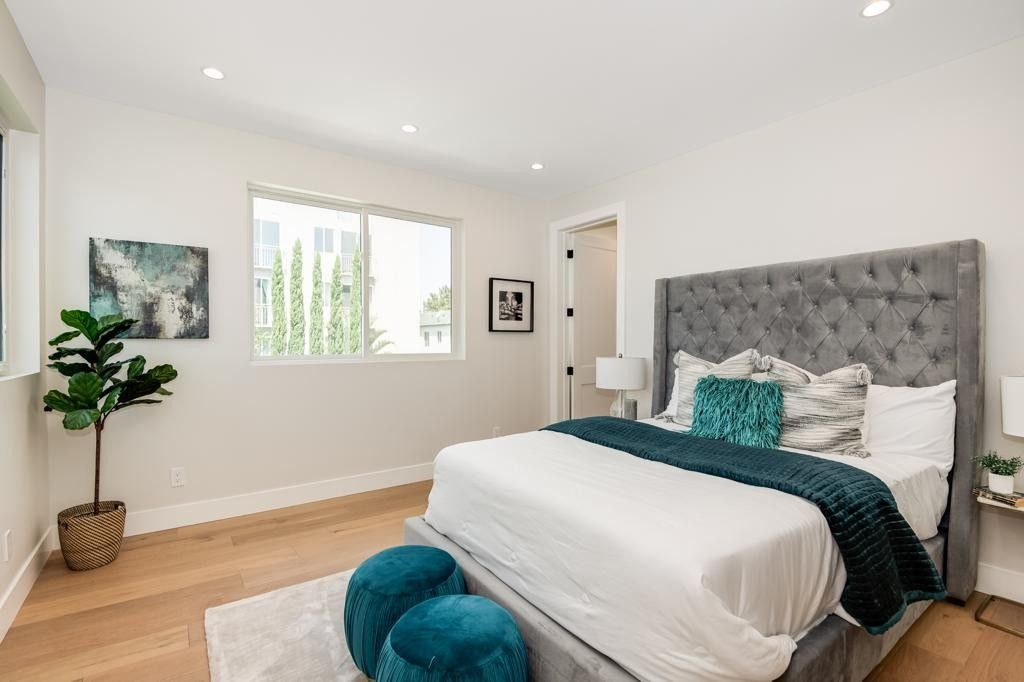 Bedroom with a tufted gray headboard, teal accents, and light wood floors.