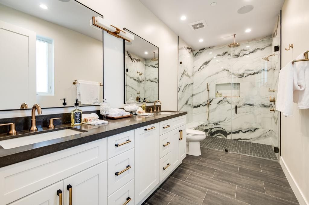 Luxurious white bathroom with black countertop, gold fixtures, and marble shower.