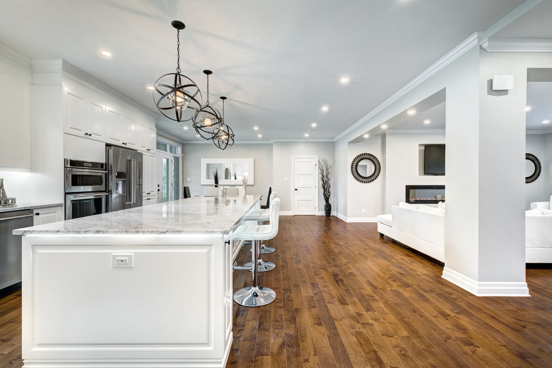 Bright, modern kitchen with white cabinetry, marble island, dark wood floors, and orb pendant lights.