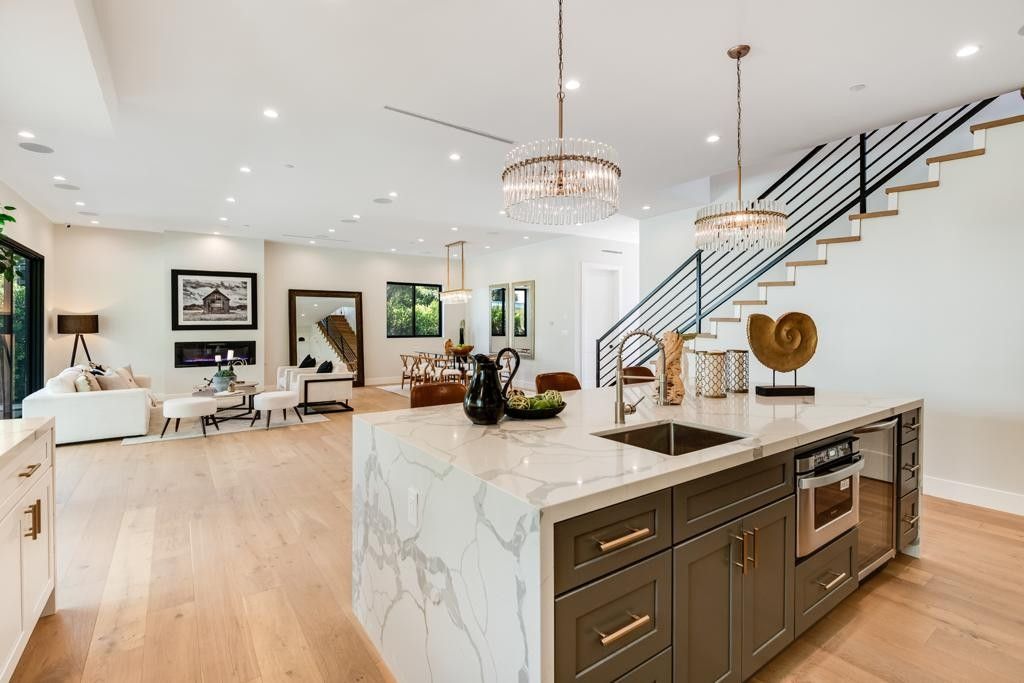 Spacious kitchen with a large island, connected to a living area and staircase. Modern design, light wood floors.