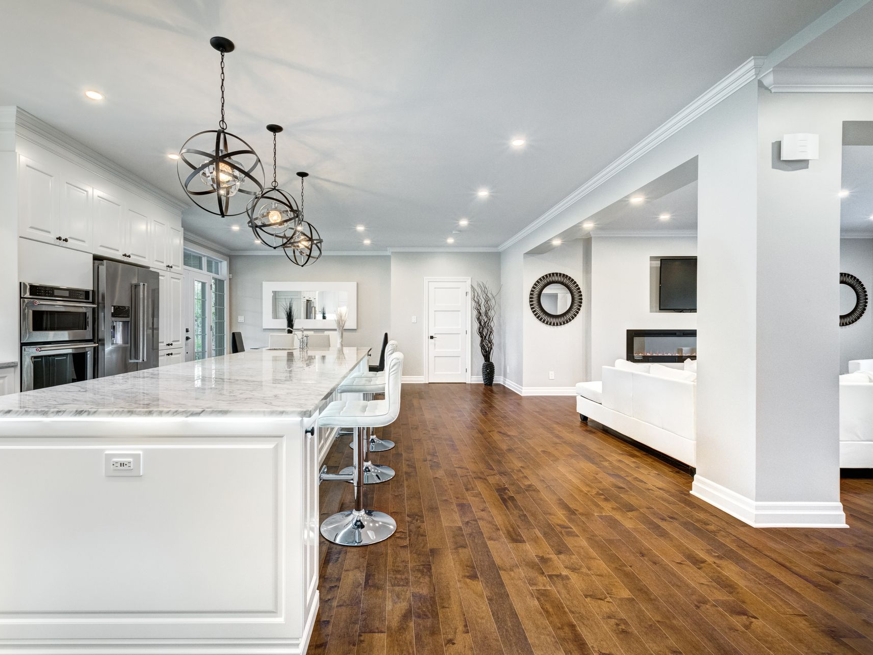 Spacious open-concept kitchen with white cabinets, marble island, dark wood floors, and modern light fixtures.