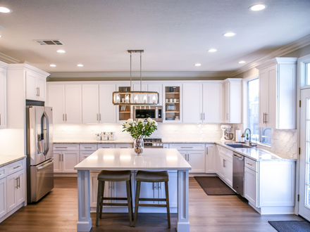 Bright white kitchen with a center island, stainless steel appliances, and wood flooring.