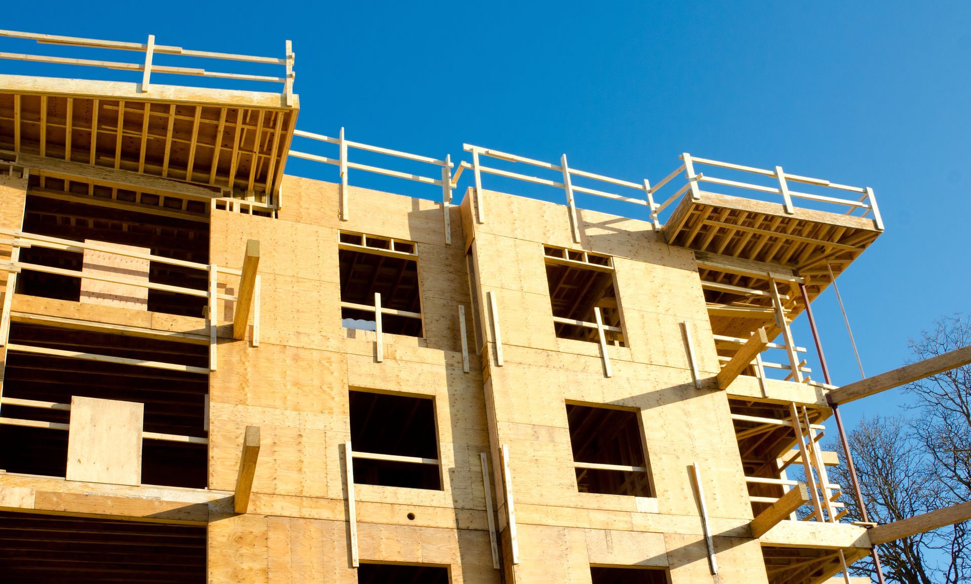 Multi-story building under construction with exposed wooden framing and blue sky.