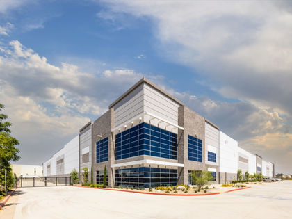 Large modern industrial building with gray and blue accents, under a cloudy sky.