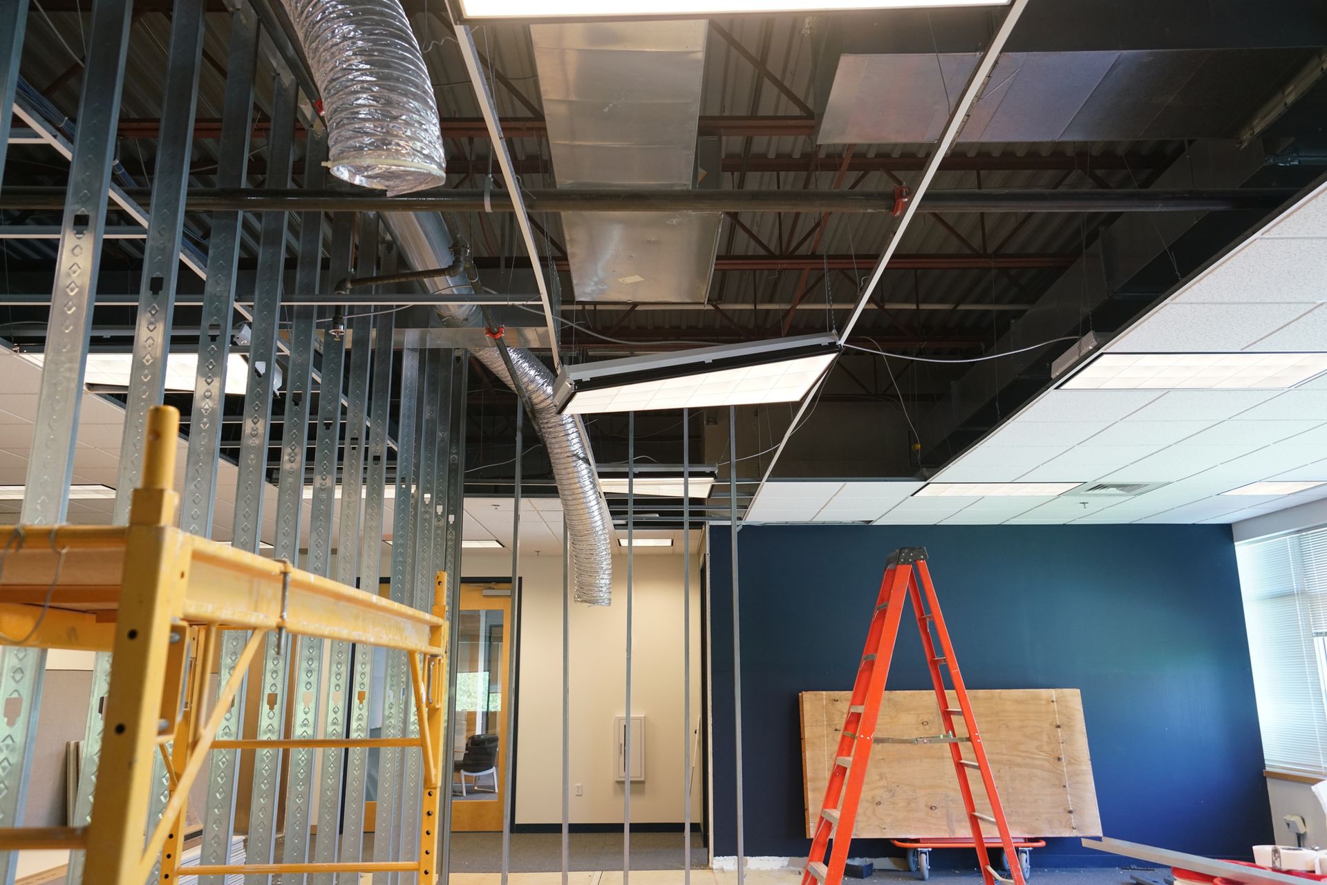Interior construction site with exposed ductwork, metal framing, and ladders.