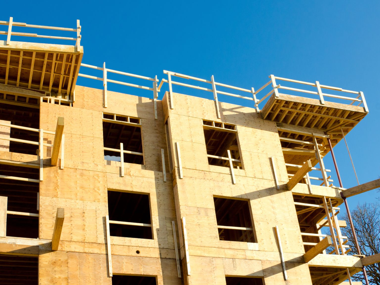 Wooden multi-story building under construction with blue sky.