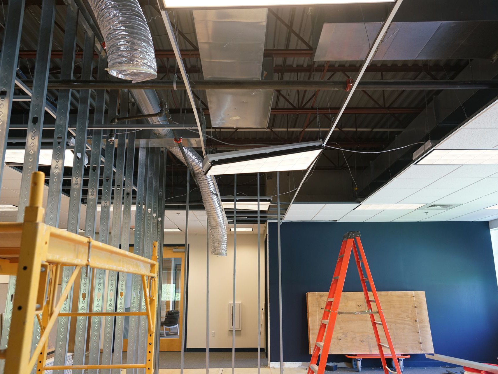 Construction site: unfinished ceiling with exposed metal framing, ductwork, and ladder.